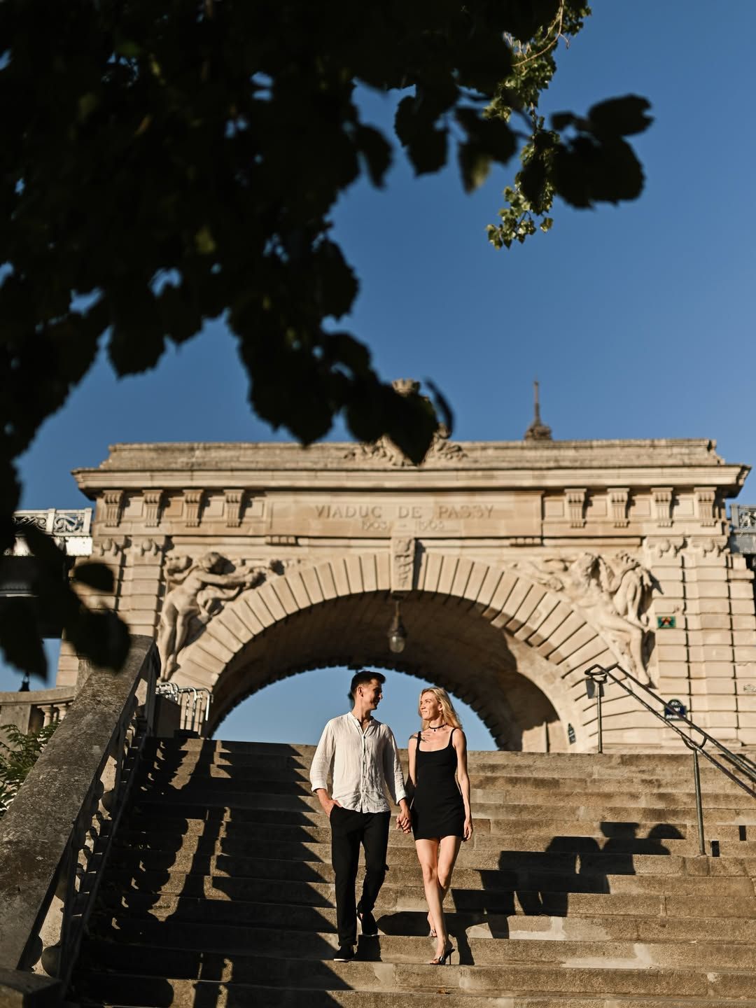 Newly engaged couple walking down stone stairs at Viaduc de Passy, taken by a surprise proposal photographer in Paris.