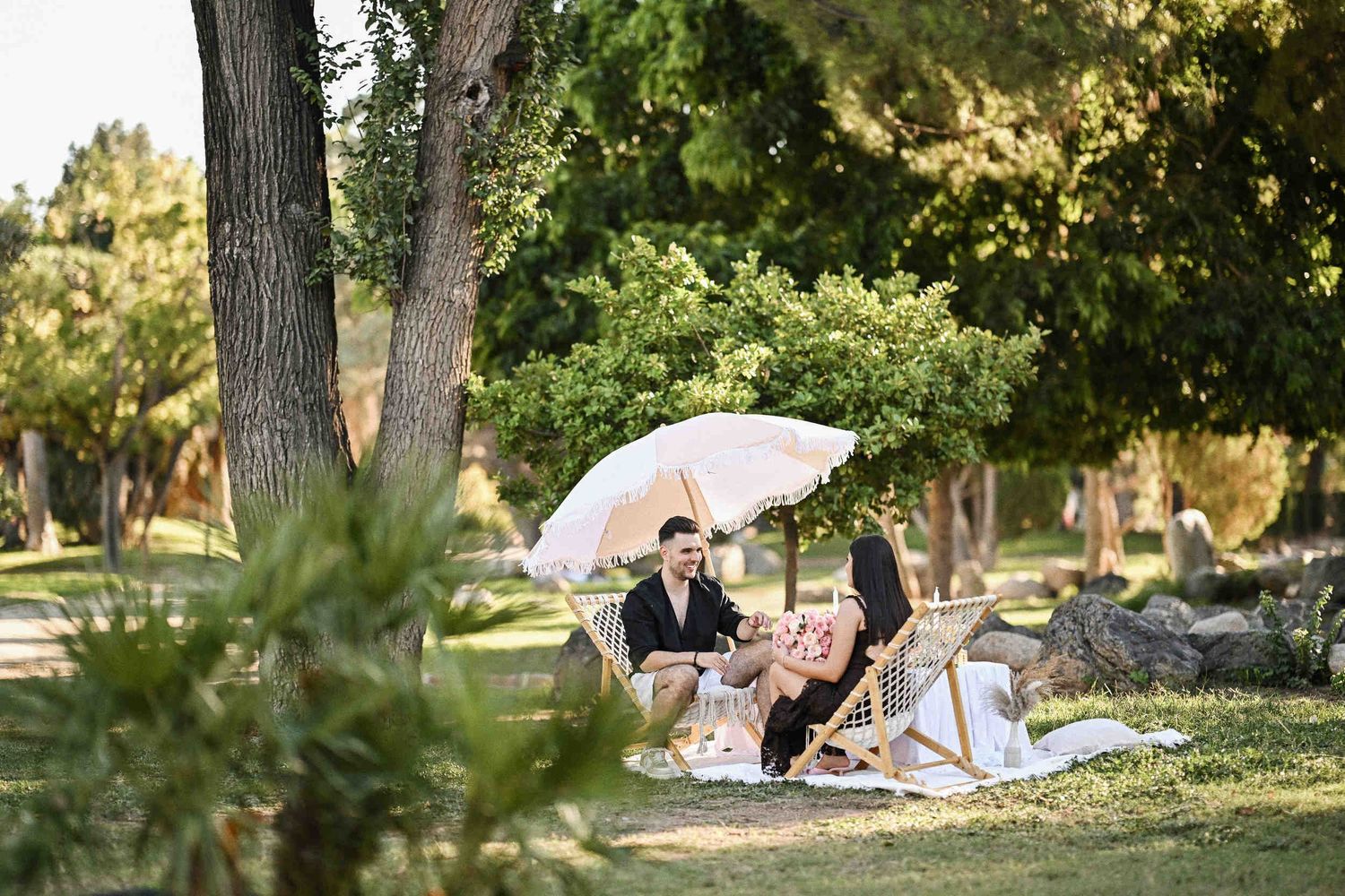 Newly proposal couple smiling under a fringed boho umbrella during their outdoor picnic in Valencia.