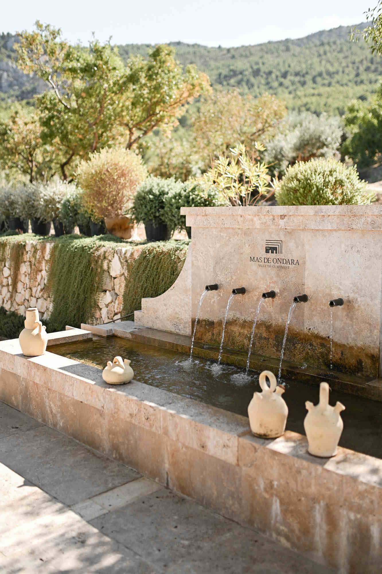 Stone water fountain with ceramic jugs and Mas de Ondara branding in the Guadalest Valley