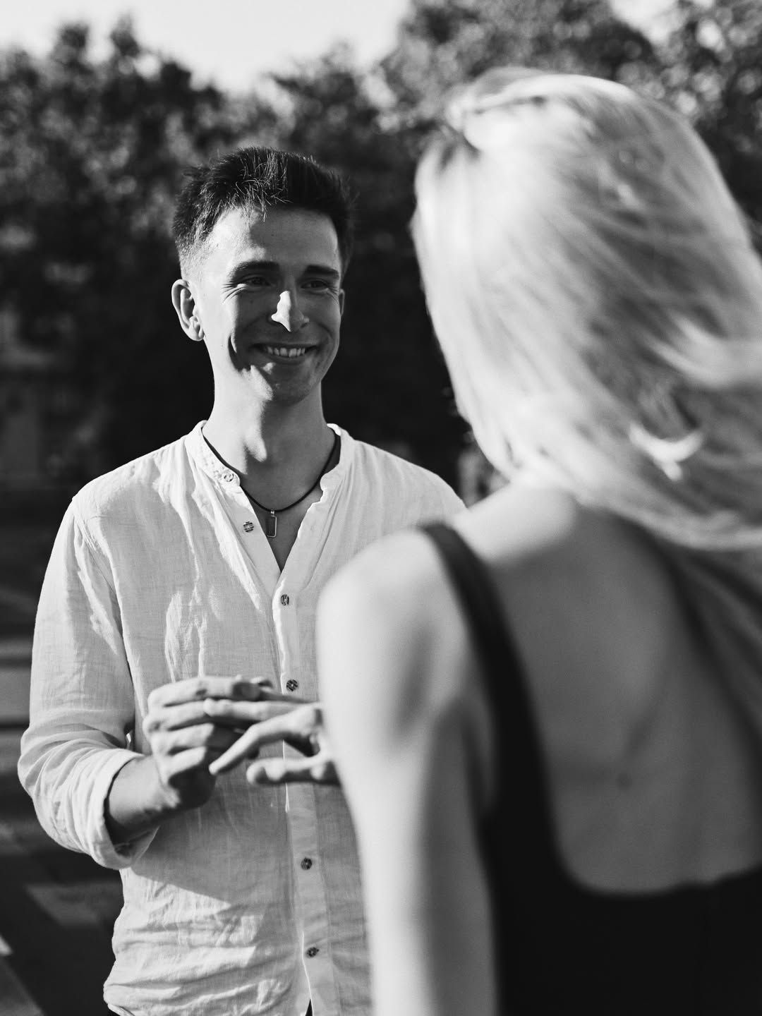 Black and white shot of a happy man smiling warmly at his fiancée just after proposing in Paris, with soft background blur.