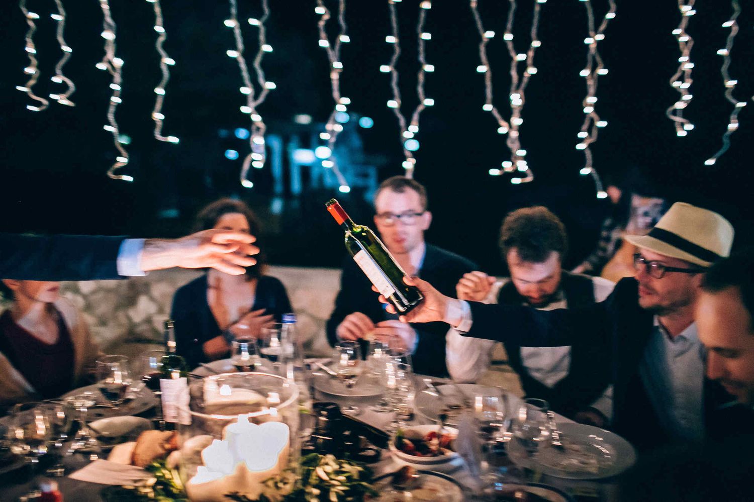 Motion blur reportage of guests passing a wine bottle at a European wedding. Captured by a documentary wedding photographer.
