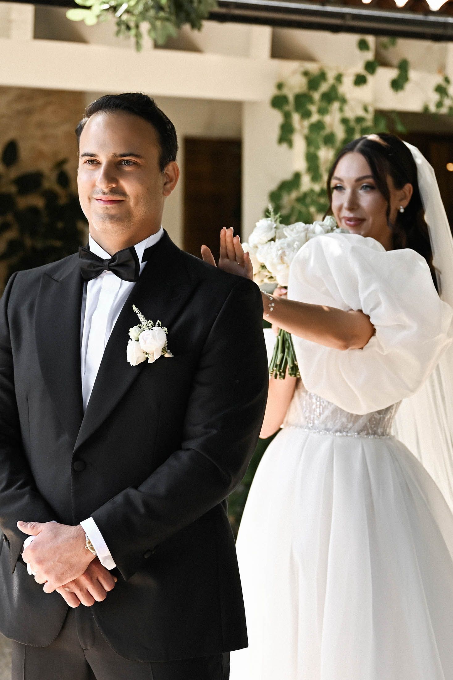 The bride gently touches the groom's shoulder to reveal her dress during intimate first look session in the Finca del Canónigo courtyard