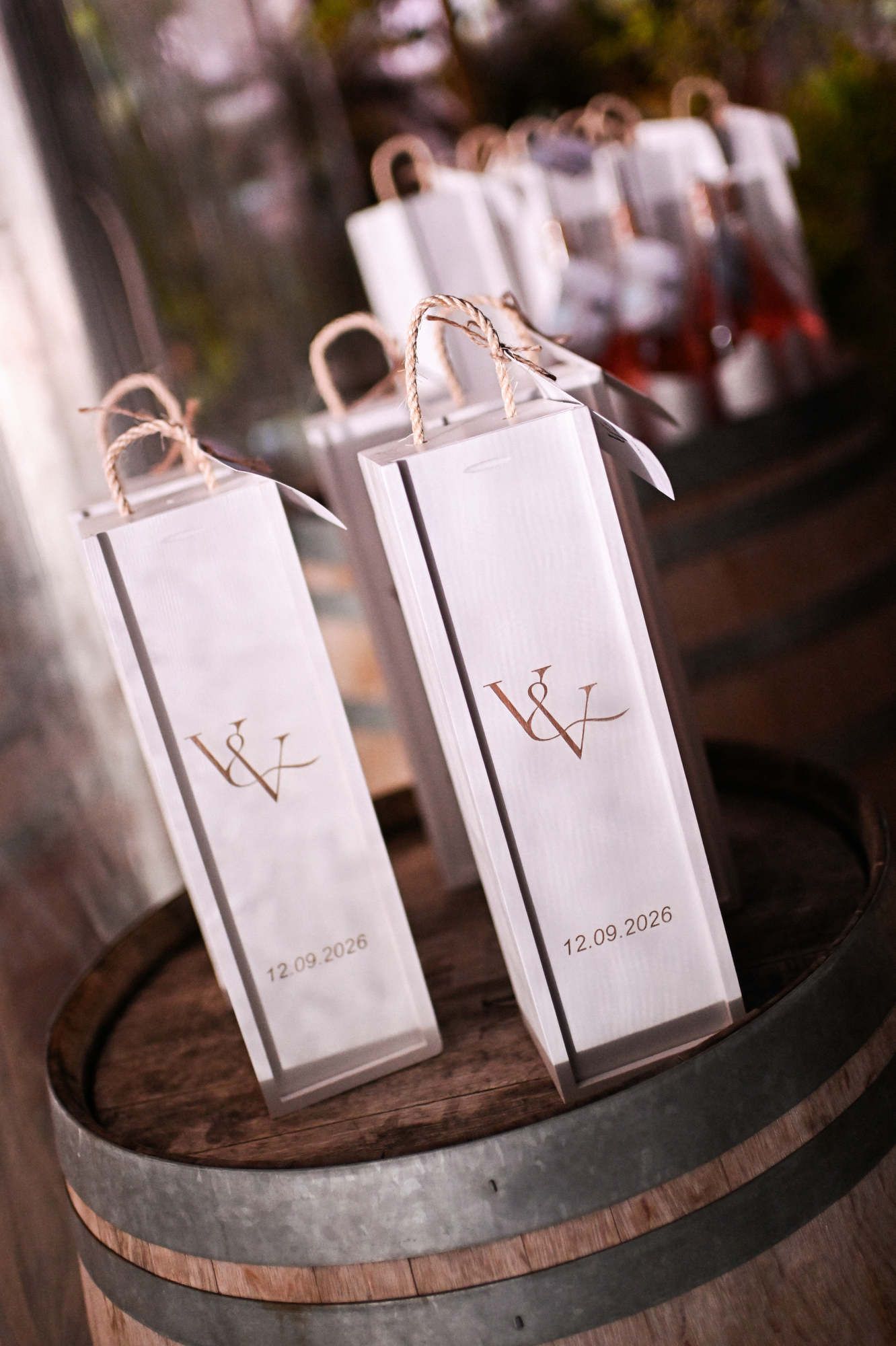 Personalized wooden wine gift boxes resting on a rustic wine barrel during a Bodega MASOS wedding.