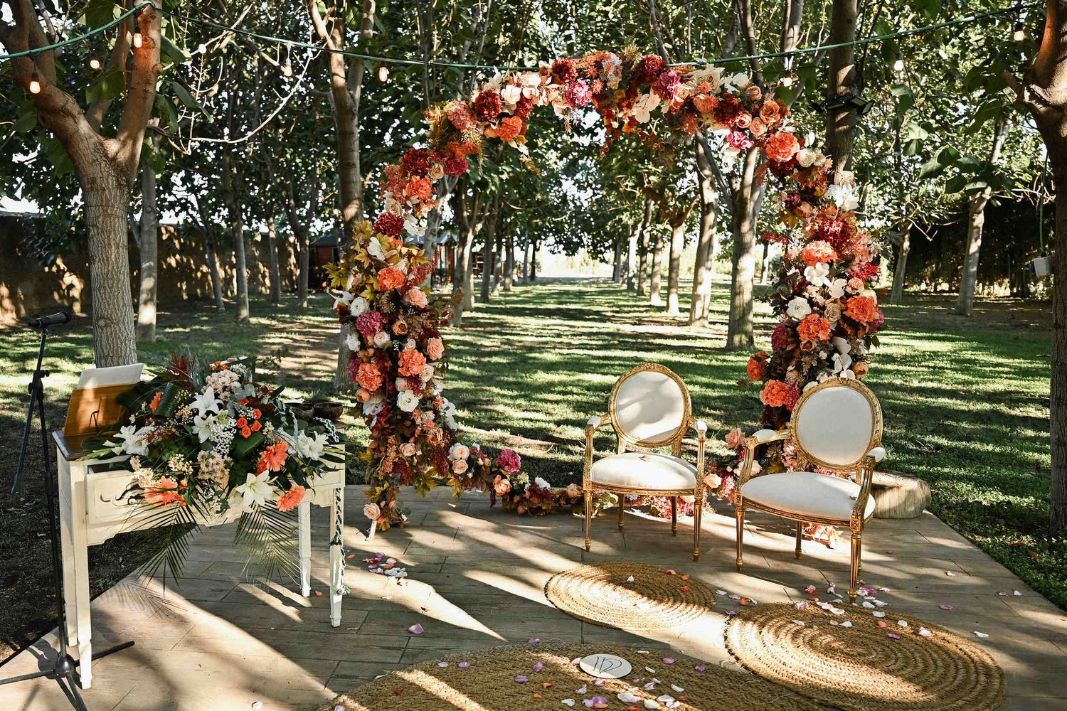 Outdoor wedding ceremony setup with a colorful floral circle arch and gold chairs at Masia El Graner.