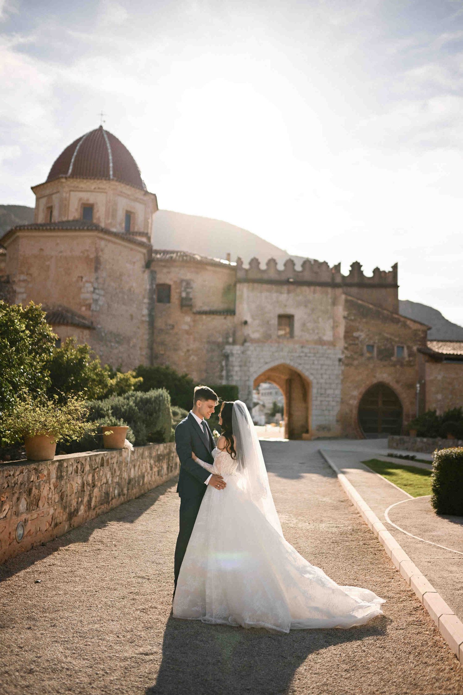 Cinematic wedding portrait of a couple at the main entrance of Monasterio de la Valldigna with majestic mountain views in the background.