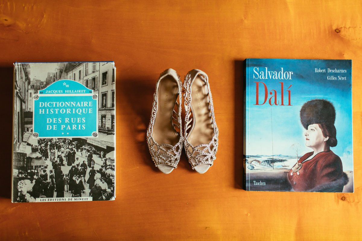 Bridal shoes placed between vintage Paris and Dali books on a wooden table before a destination wedding at Chateau de Changy.