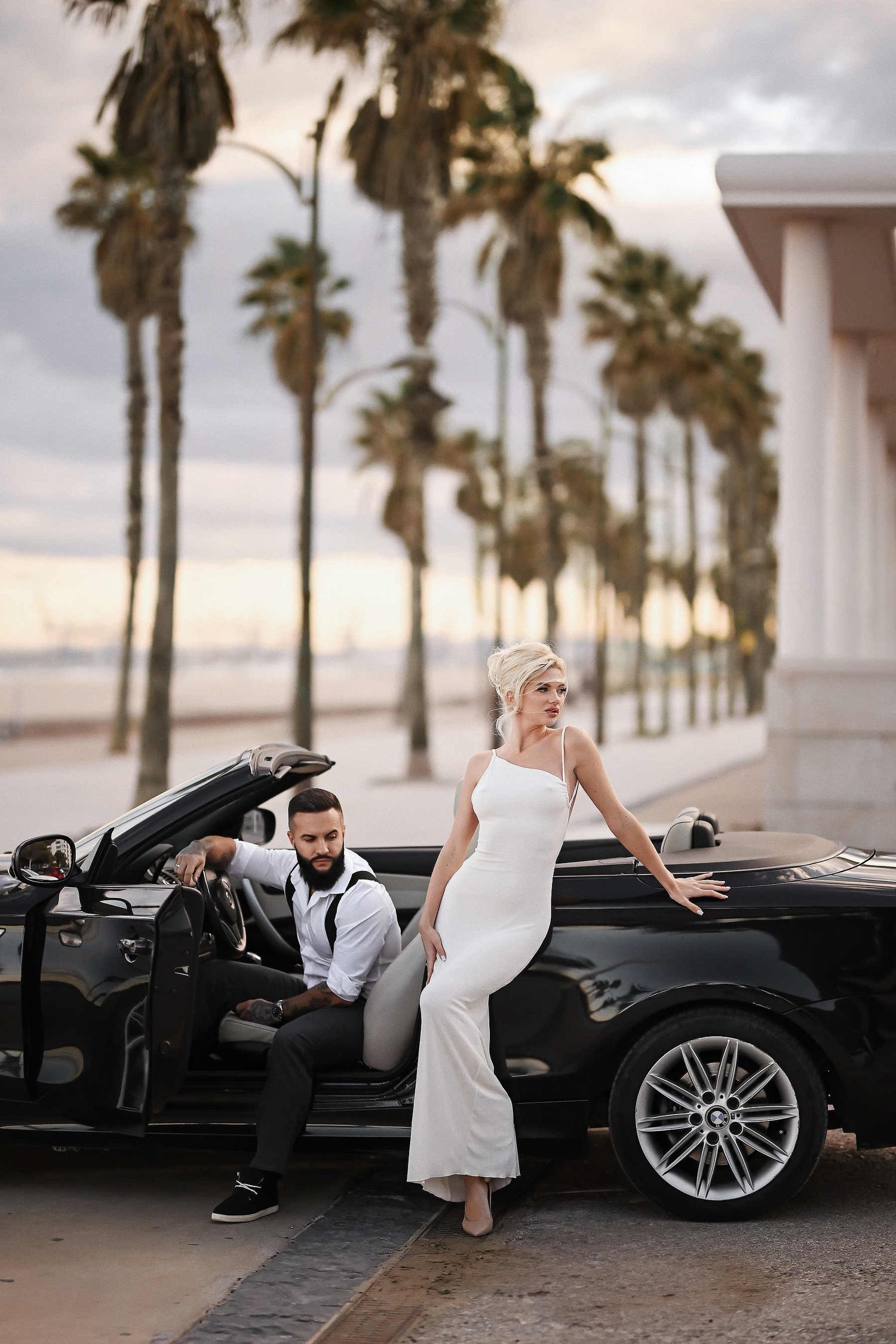 Luxury wedding in Spain. A stylish couple posing in a vintage sports car on the sea embankment along the scenic Mediterranean coast