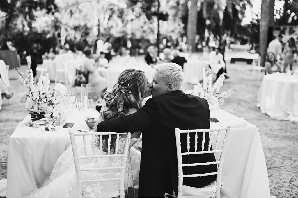Back view of the newlyweds kissing at the dinner table with all the wedding guests in the background at Finca El Senyoret, Benidorm.