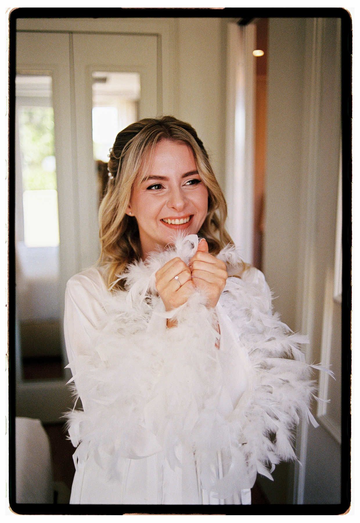 Bride in a feather robe hugging herself and smiling with bridesmaids, shot on film at Finca El Senyoret.