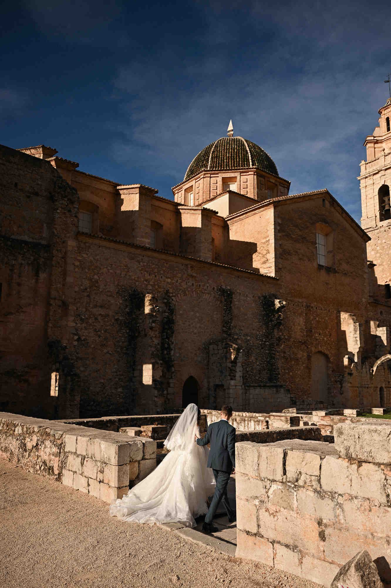 Bride in a beautiful wedding dress and groom entering the historic outdoor buildings of the Monasterio de Santa María de la Valldigna.