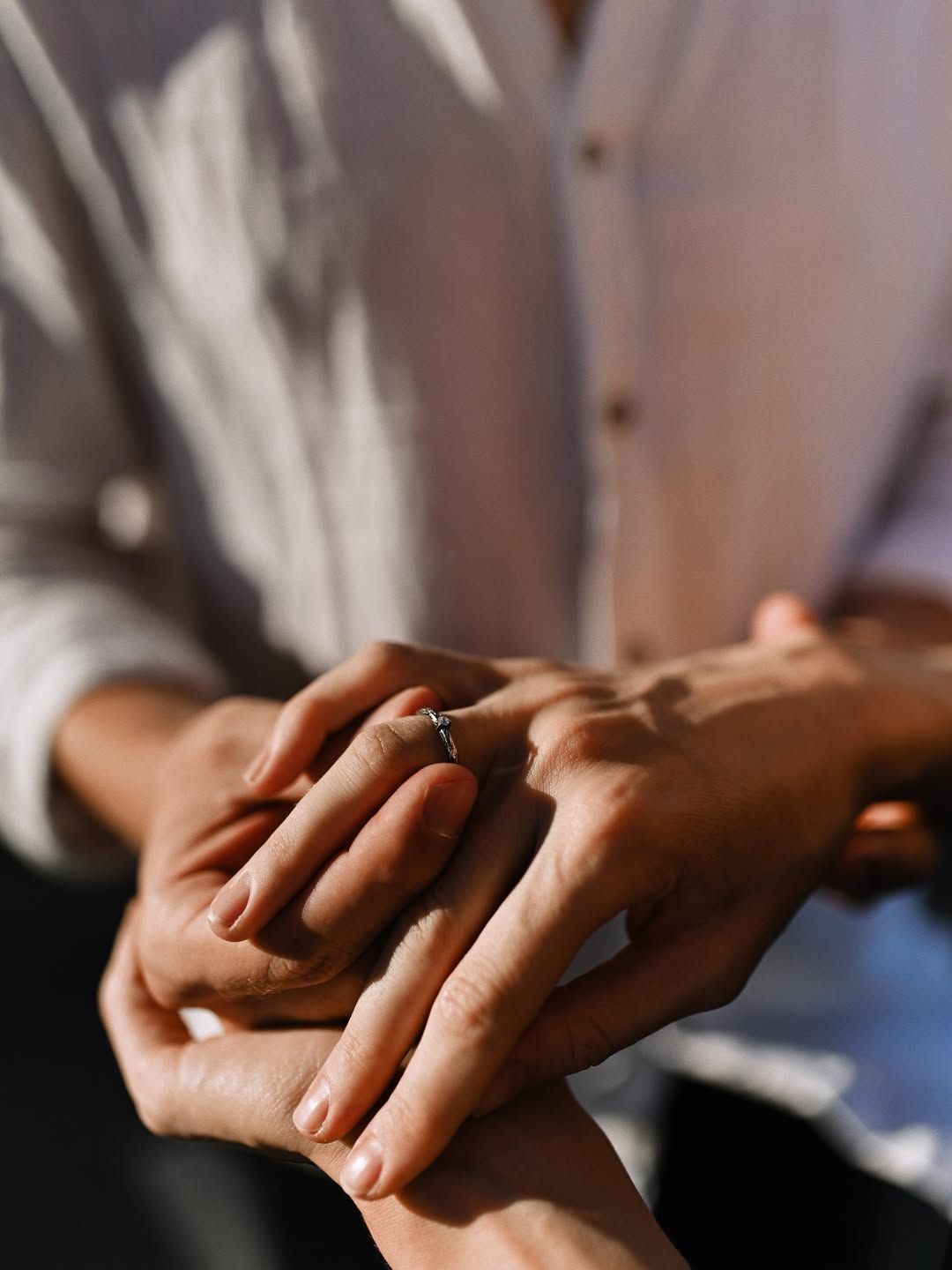 Close-up of a man sliding a diamond engagement ring onto his partner's hand in warm evening sunlight in Paris.