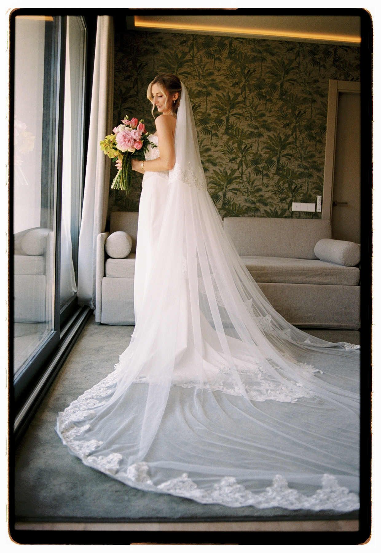 Full-length portrait of a bride during morning prep, showing her stunning wedding dress and long veil.