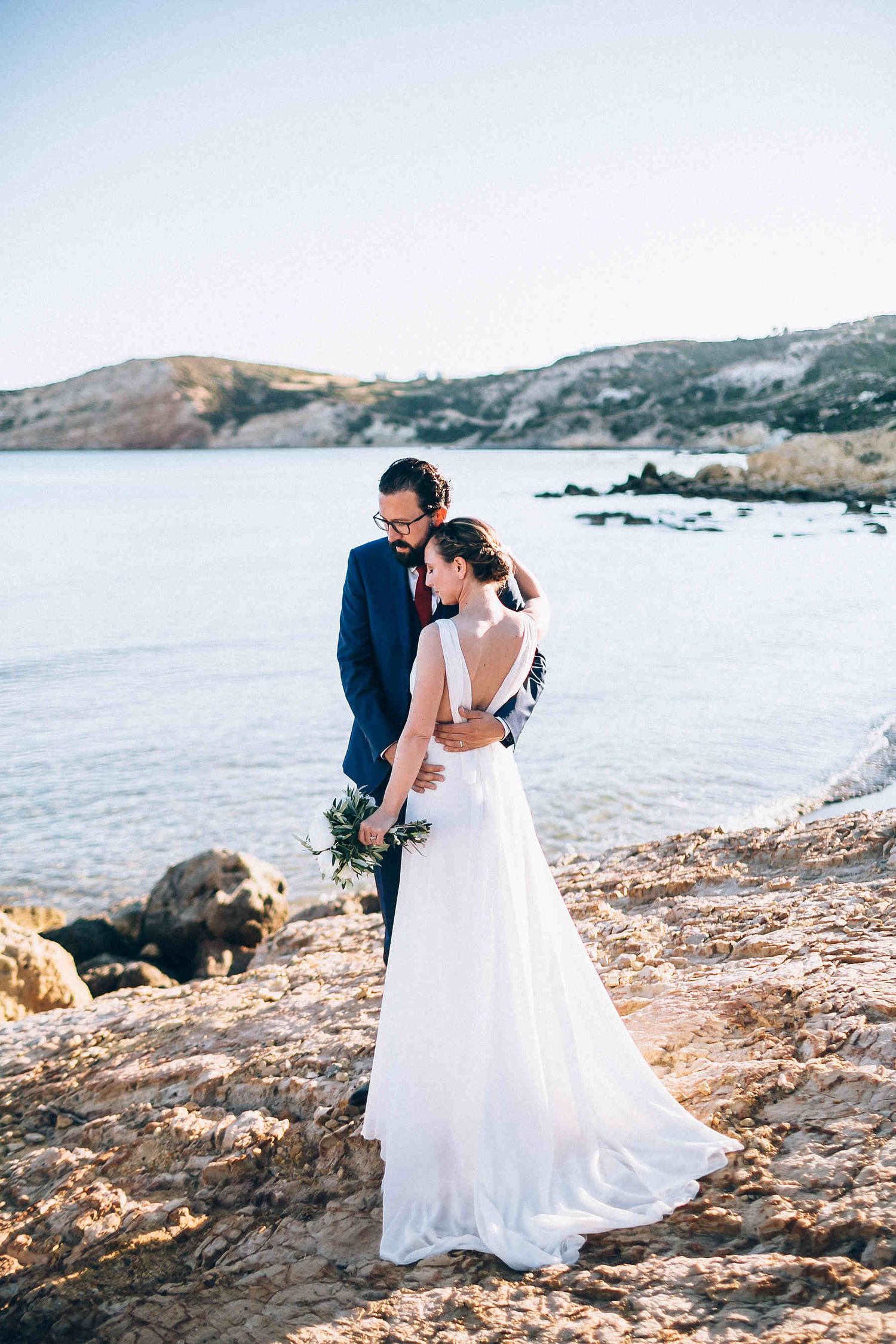 Bride and groom portrait with a long dress train flowing on the windy beach in Greece