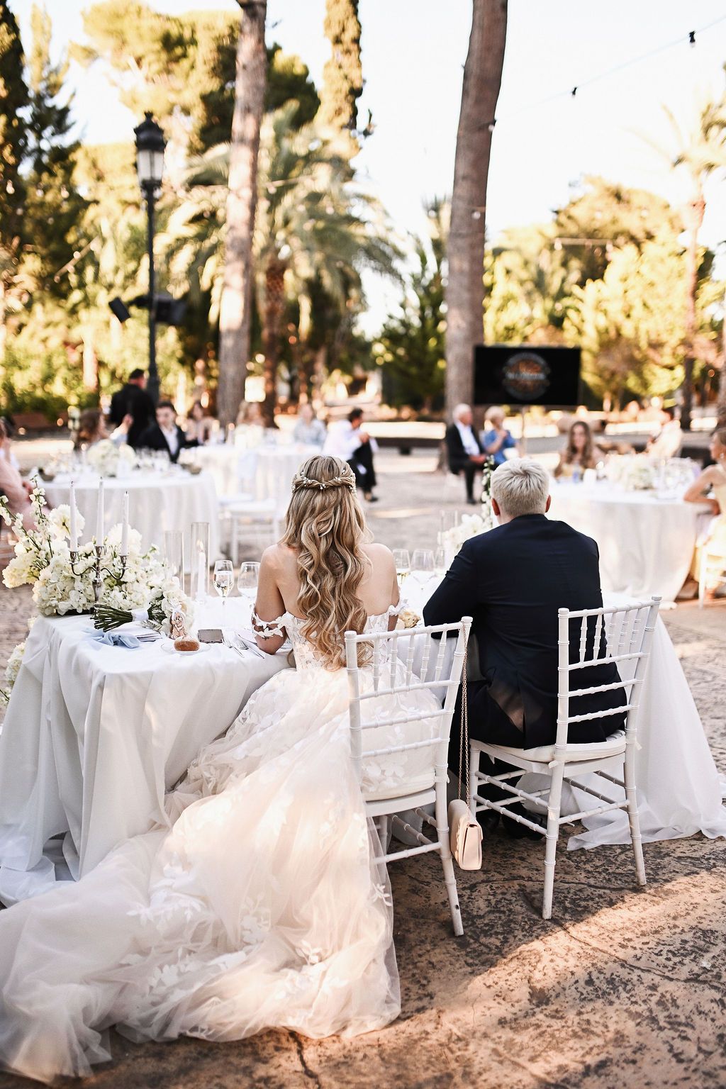 Back view of bride and groom sitting at the open-air dinner table under string lights at a luxury wedding venue in Benidorm.