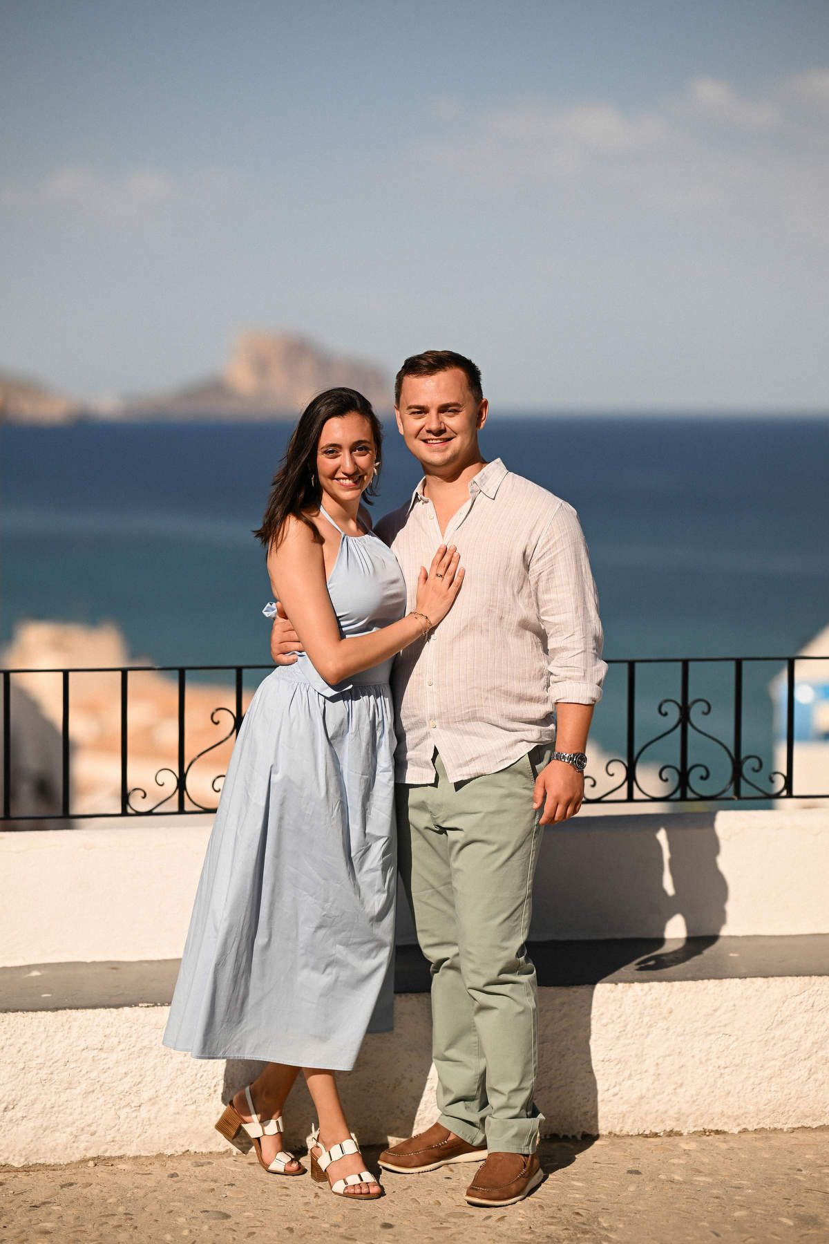A smiling woman rests her hand on her partner's chest to show her new ring after a surprise marriage proposal in Altea.