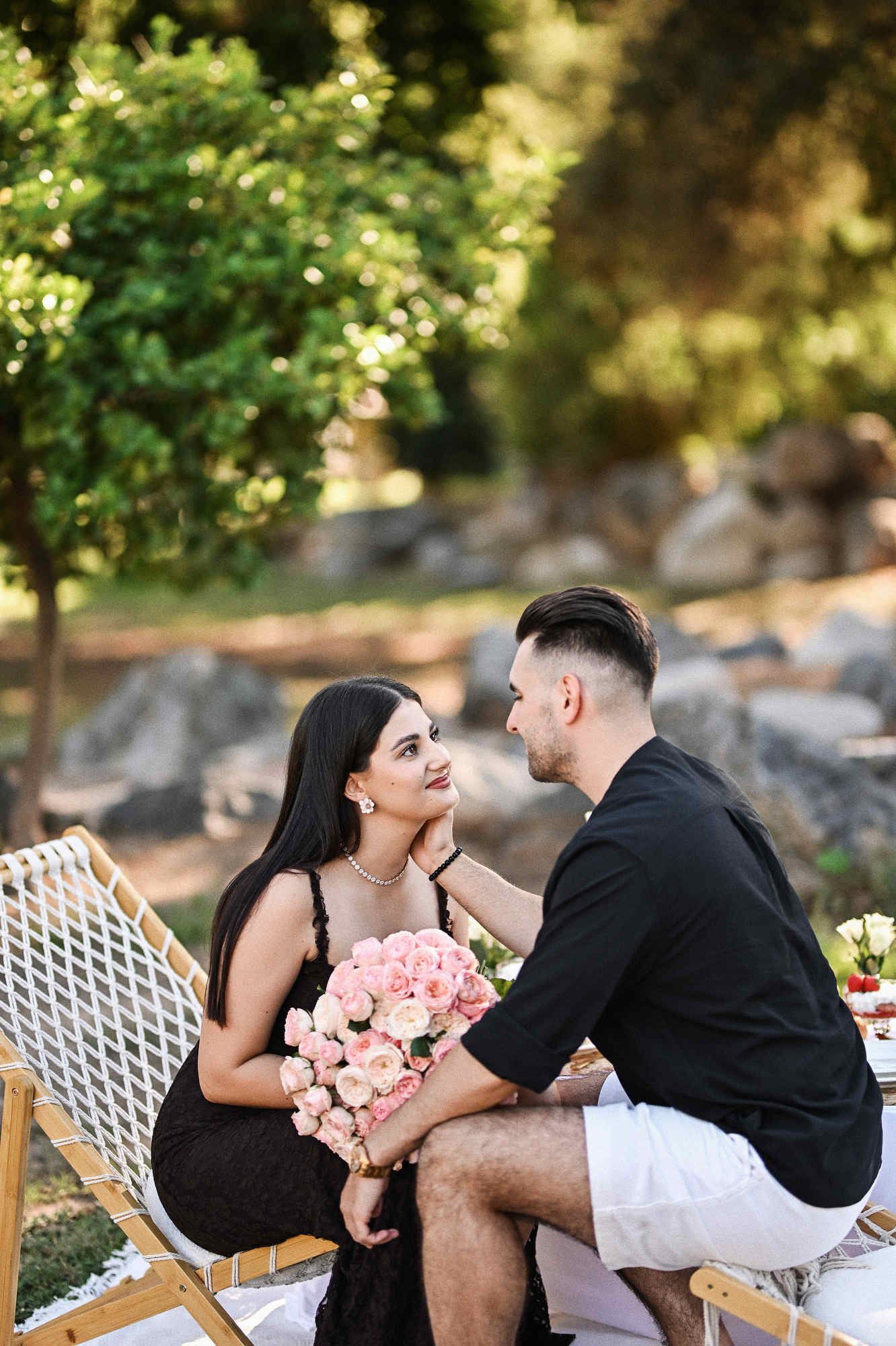 Newly engaged couple looking affectionately at each other with a pink rose bouquet at their Viveros Park picnic.