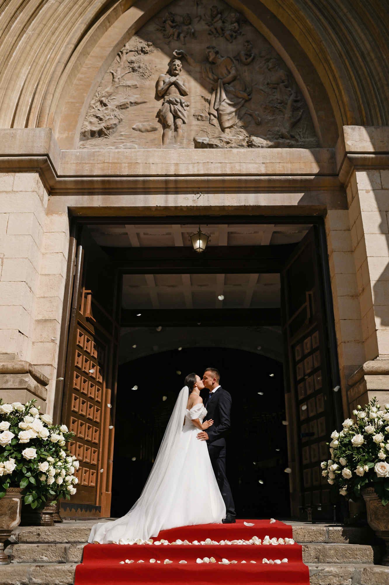 Bride and groom kissing at the entrance of a historic church in Valencia, framed by beautiful, grand architectural gates.