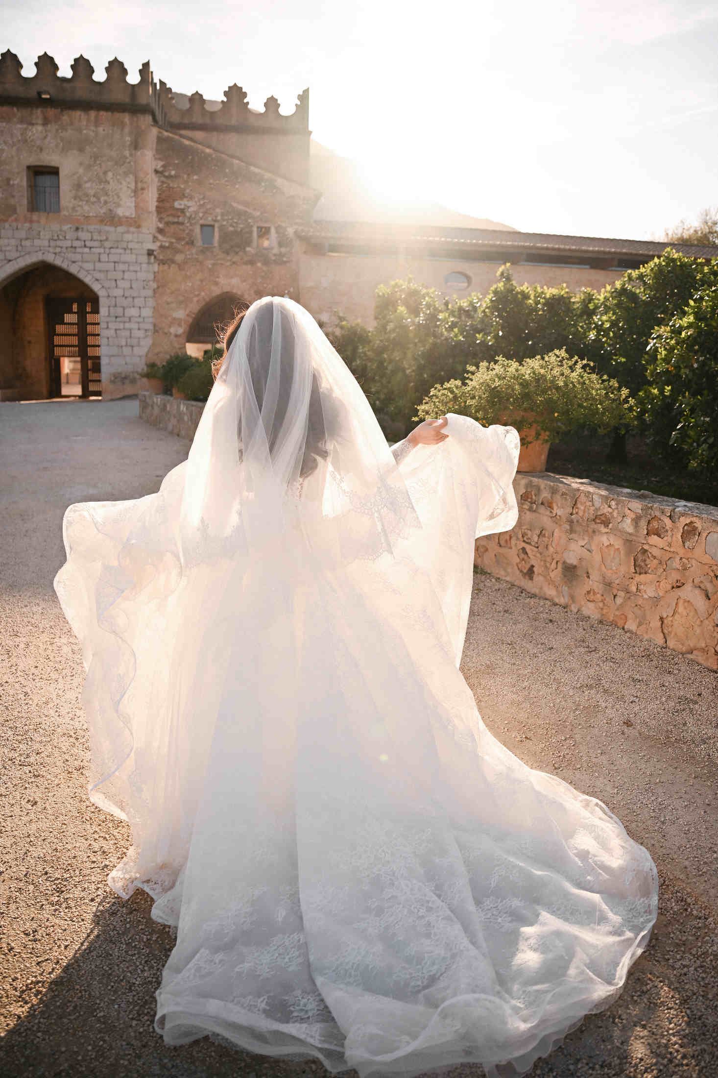 Bride walking away dynamically, showing the elegant wedding dress train and veil against the walls of Monasterio