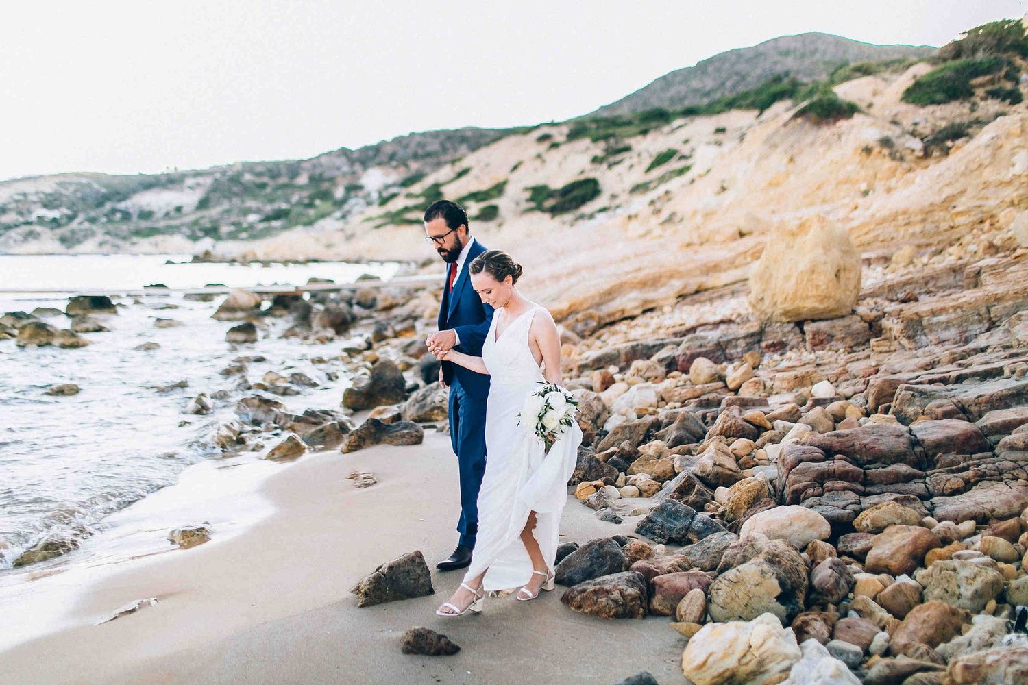 Wedding couple walking on Milos beach during wedding photo session. Professional wedding photographer Milos. Milos wedding photography.