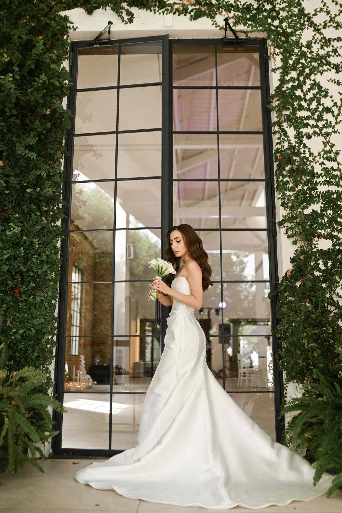 Bride posing by the grand glass entrance doors of the reception hall at El Telar. High-end destination wedding style by Darista