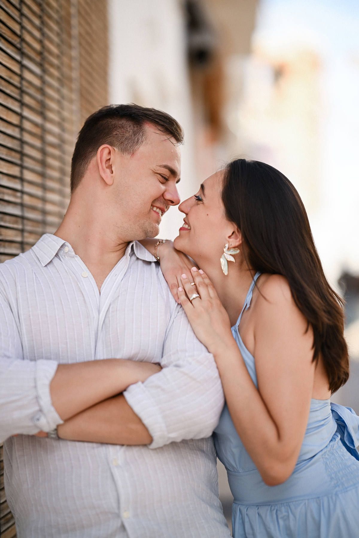 A woman in a light blue dress rests her arm on her partner's shoulder, smiling warmly during an Altea engagement shoot.