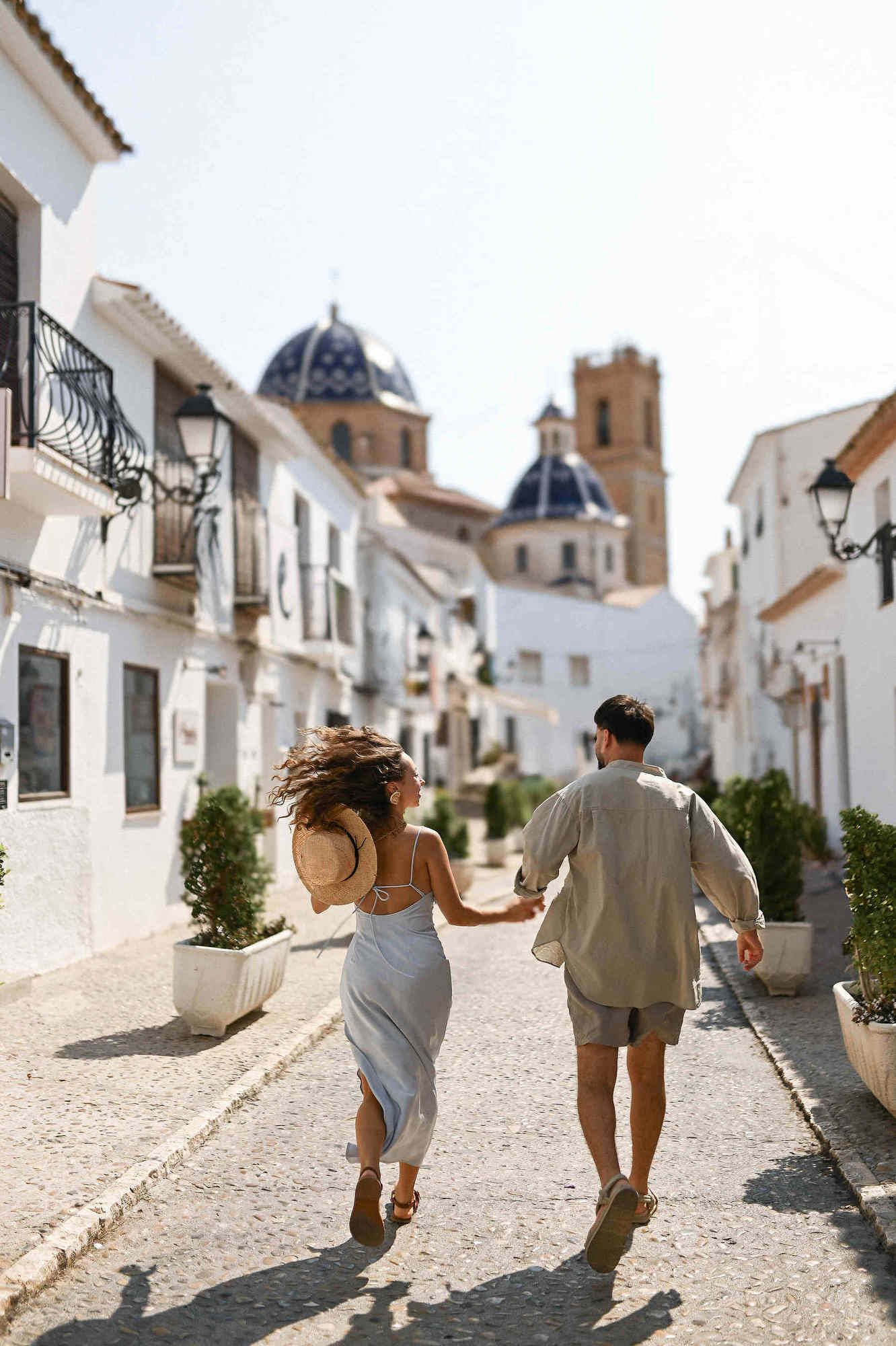 Surprise proposal photographer Spain. A joyful couple running through the streets with a majestic Spanish cathedral in the background.