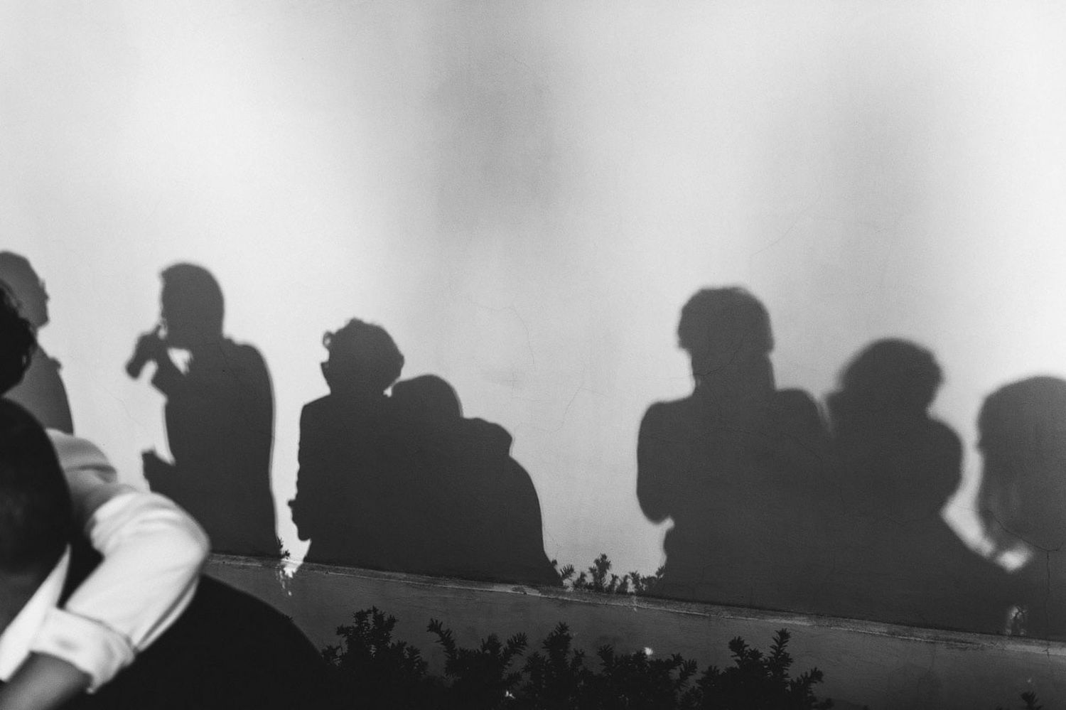 Artistic shadow play of guests enjoying cocktails and beer on a wall during a wedding reception. Captured by a European artist.