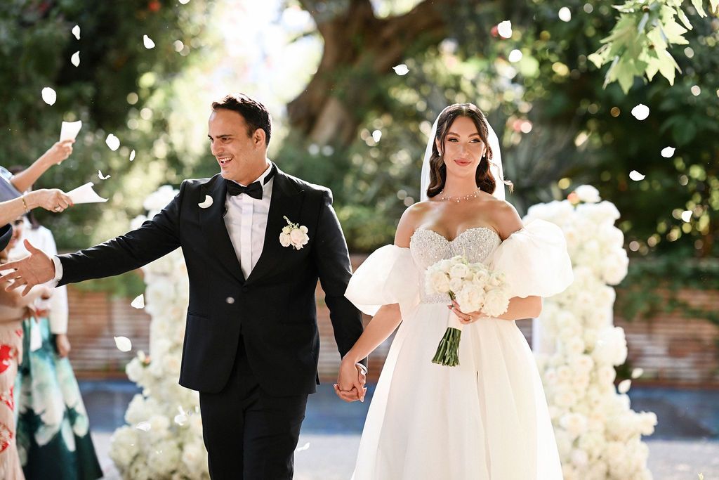 the bride and groom walking through a corridor of cheering guests tossing red rose petals during a luxury wedding at Finca del Canónigo.