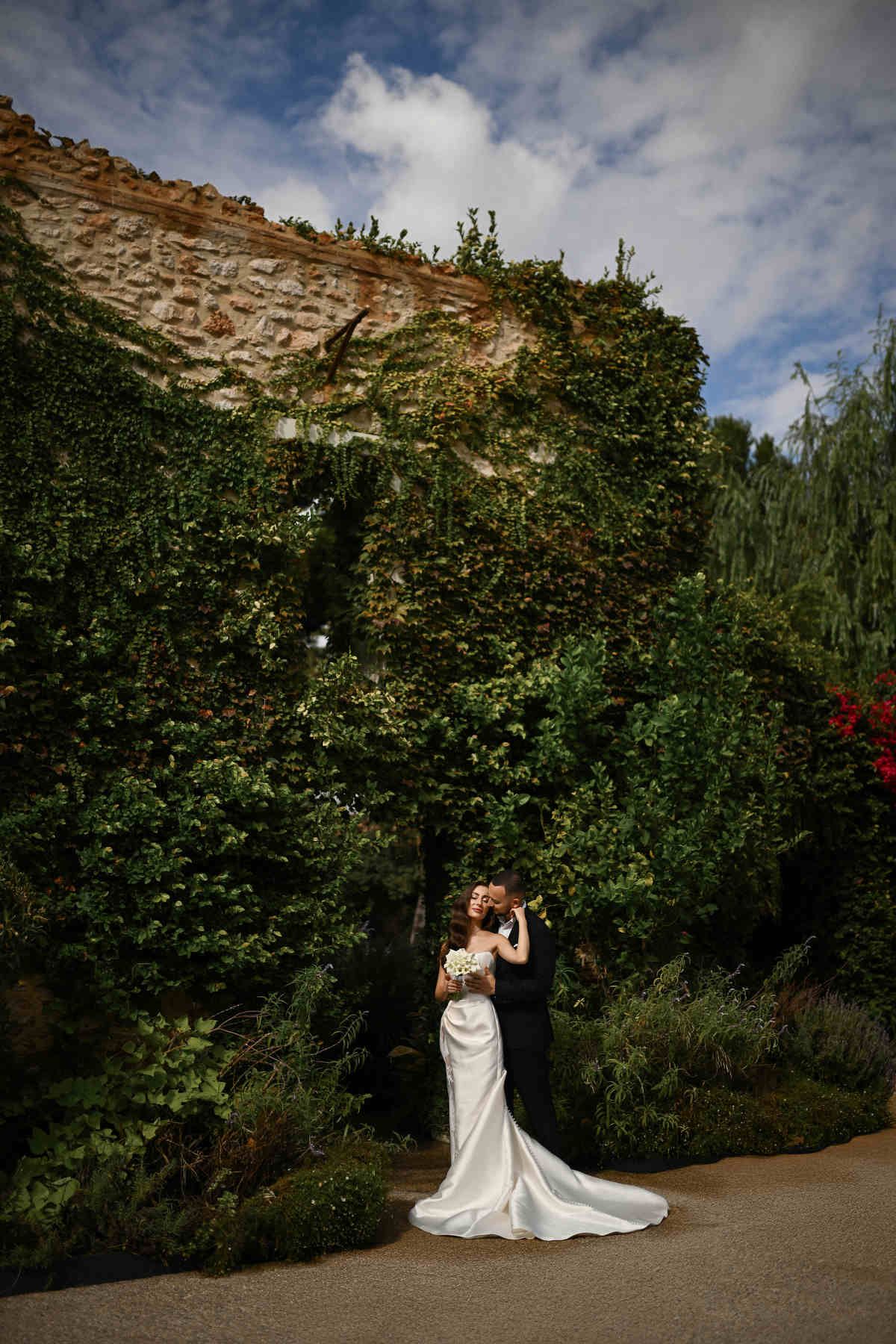 Bride and groom embracing against a lush green ivy wall at the El Telar estate. Timeless Mediterranean romance captured by Darista