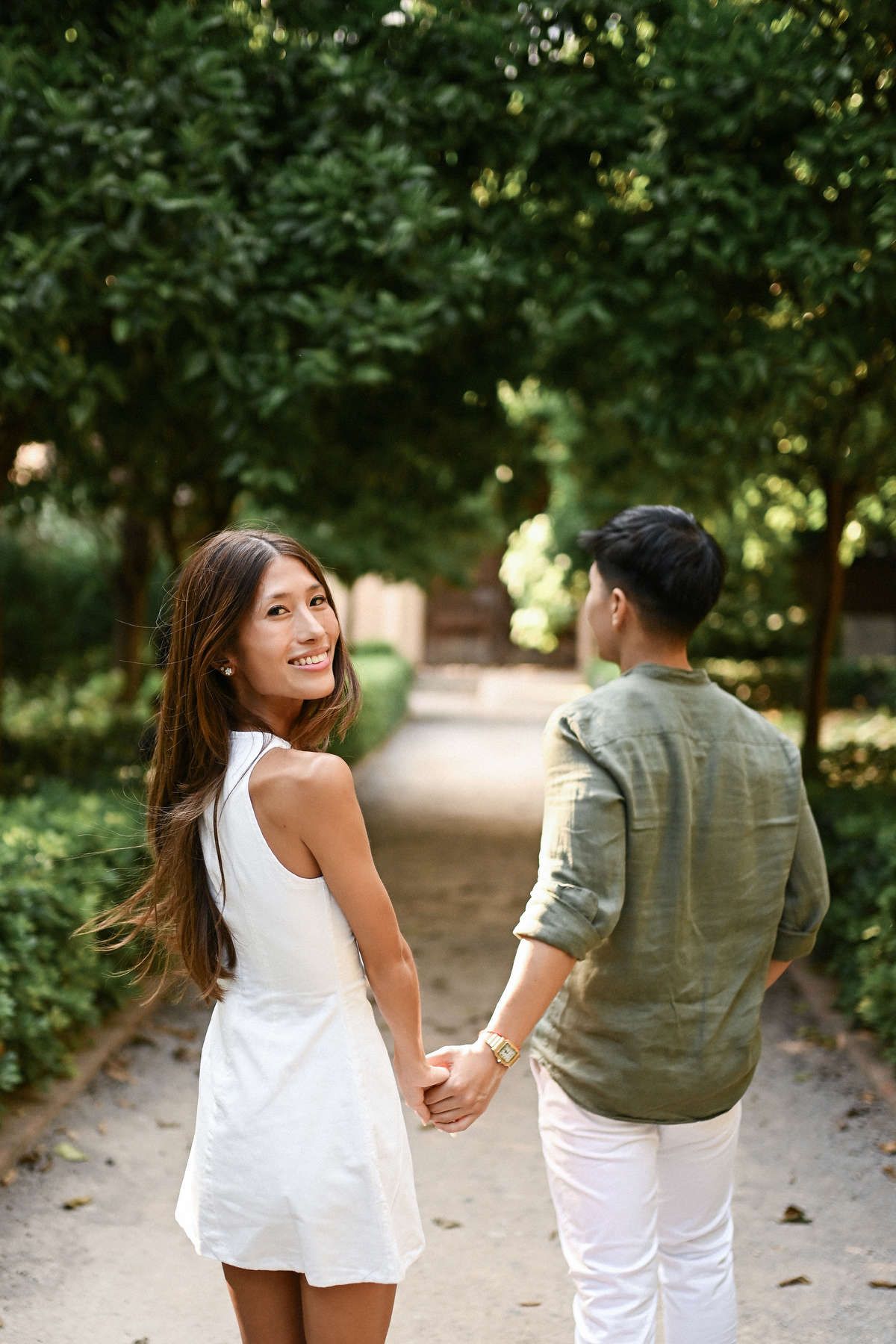 An international couple walks away holding hands on a shaded dirt path in Monforte following a private marriage proposal.