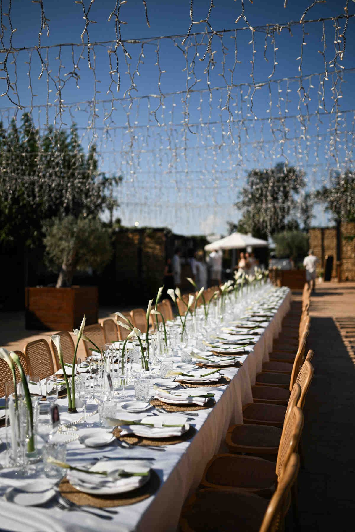 Alfresco wedding dinner setup at Alquería Kukala in Valencia with elegant tableware and hanging string lights.