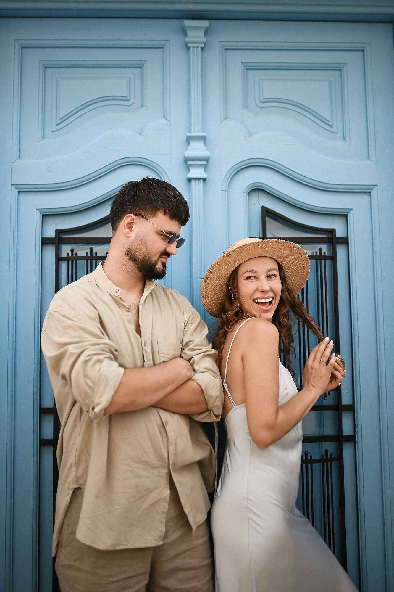 Love story photoshoot Spain. A woman smiles at her partner standing in front of a rustic, typical wooden door on a Spanish street.