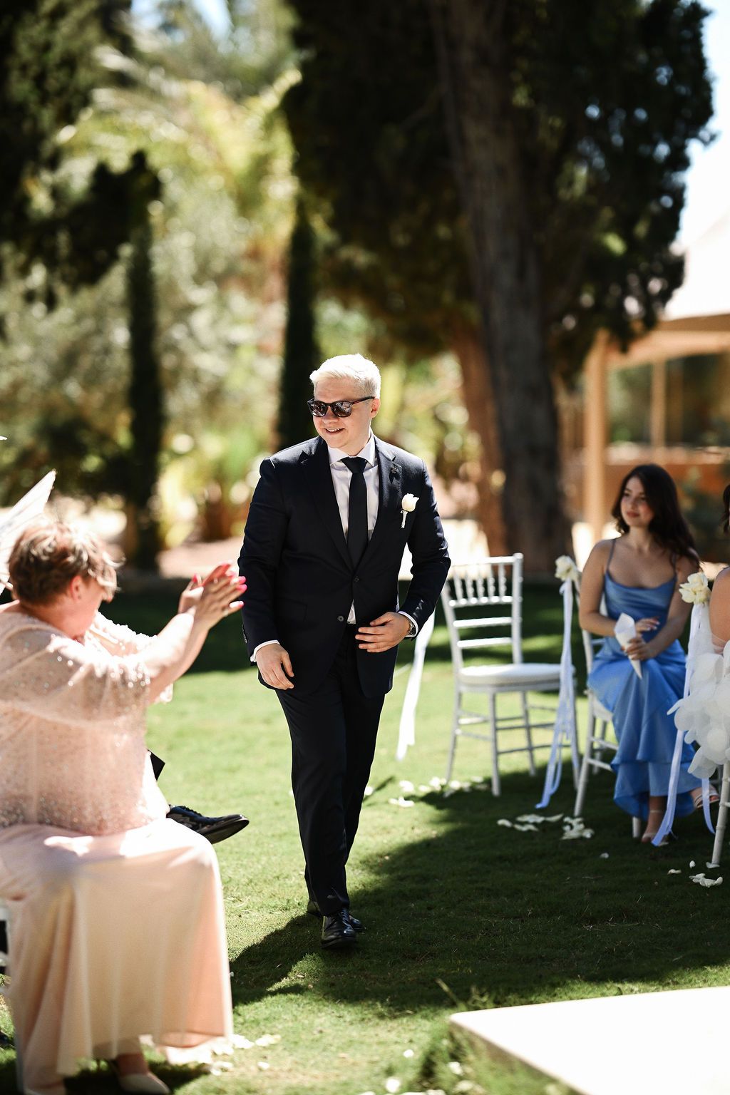 The groom walking down the aisle through the wedding guests towards the stone arch at Finca El Senyoret for a Benidorm ceremony.