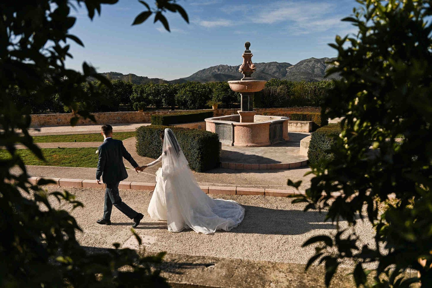 Bride and groom walking by the ornate stone fountain at Monasterio de Santa María de la Valldigna, a classic Valencian landmark backdrop.