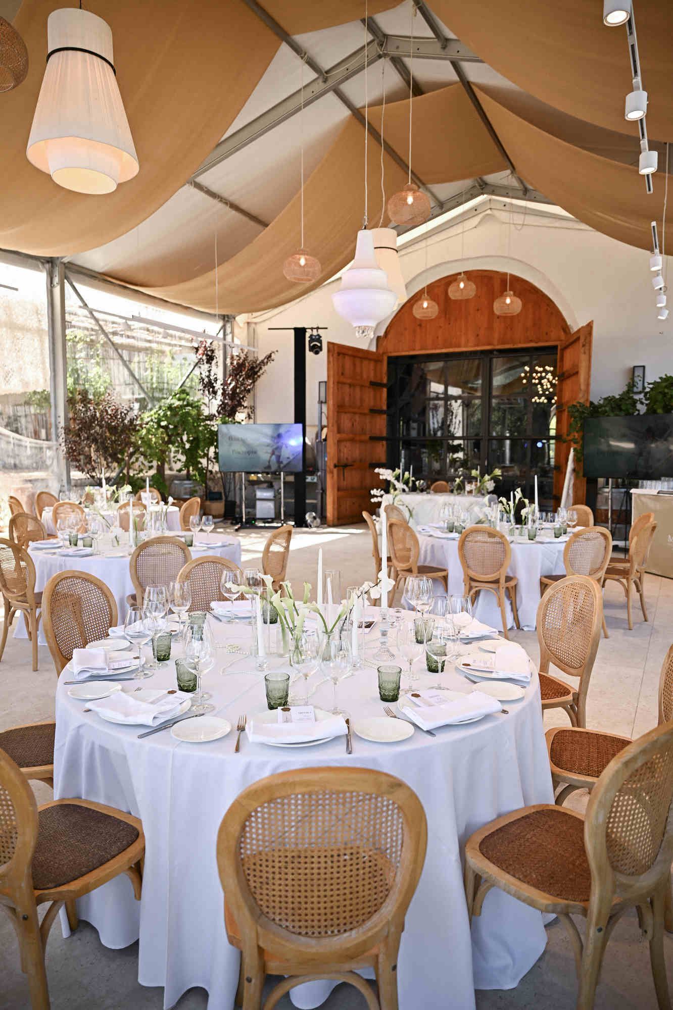 Glass-fronted banquet hall elegantly set for a winery wedding dinner with round tables and cane chairs.