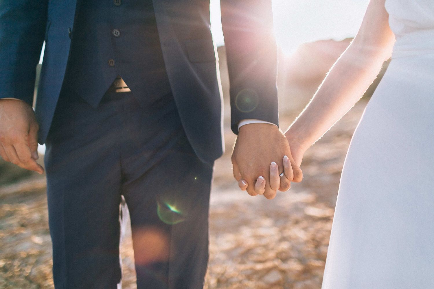 Artistic close-up of the couple's hands with warm golden hour sunlight and lens flare