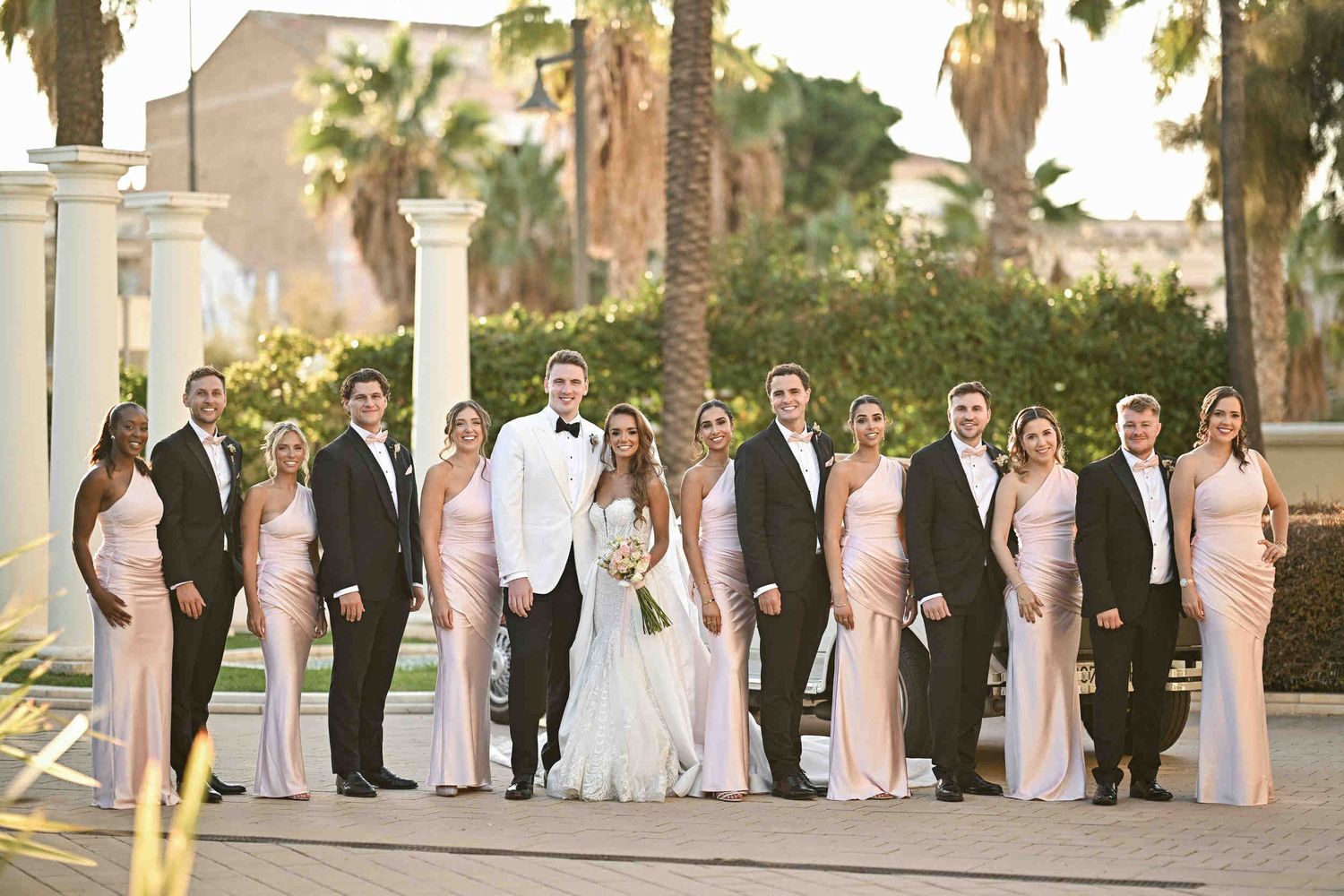 Formal group portrait of a bride and groom surrounded by their wedding party in the gardens of Hotel Las Arenas