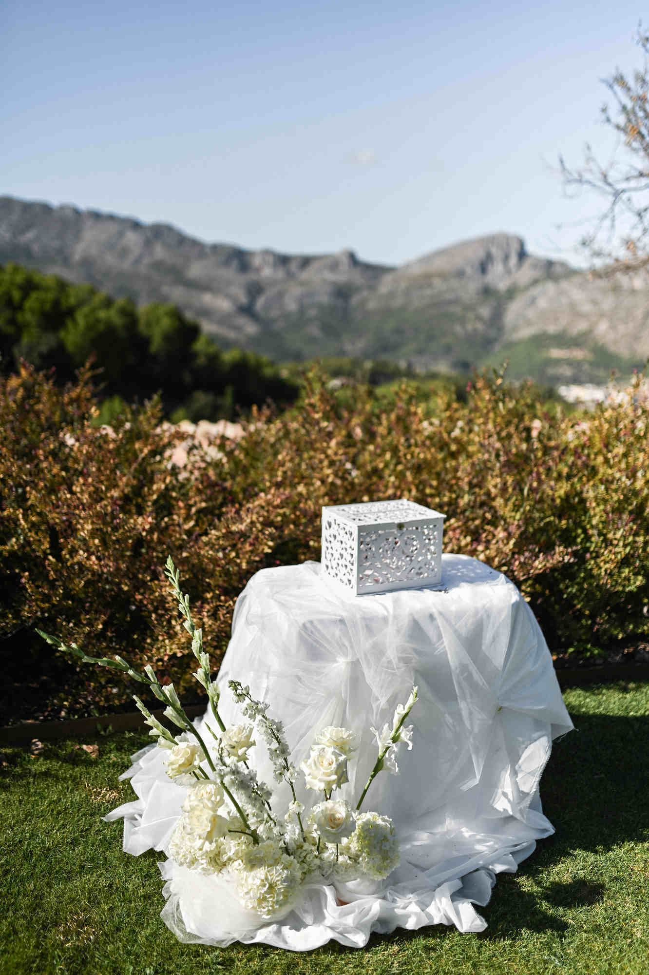 Wedding gift box table covered in white tulle and floral arrangements with mountains background.