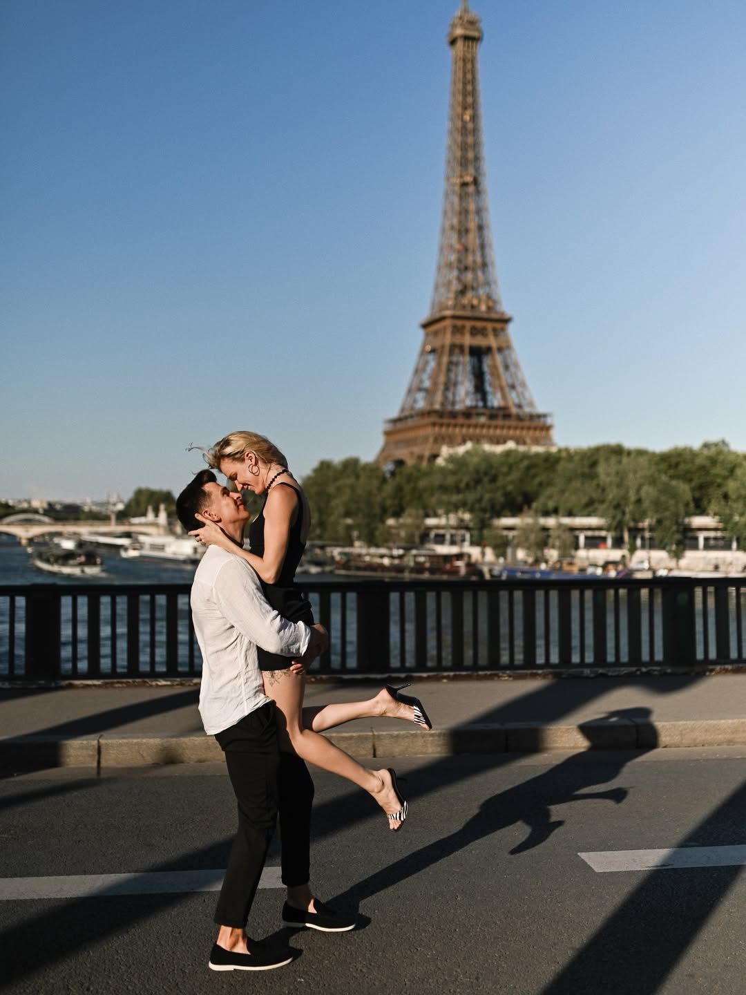 Happy man lifting his newly engaged partner on Pont de Bir-Hakeim, with sharp evening shadows and the Eiffel Tower in back.