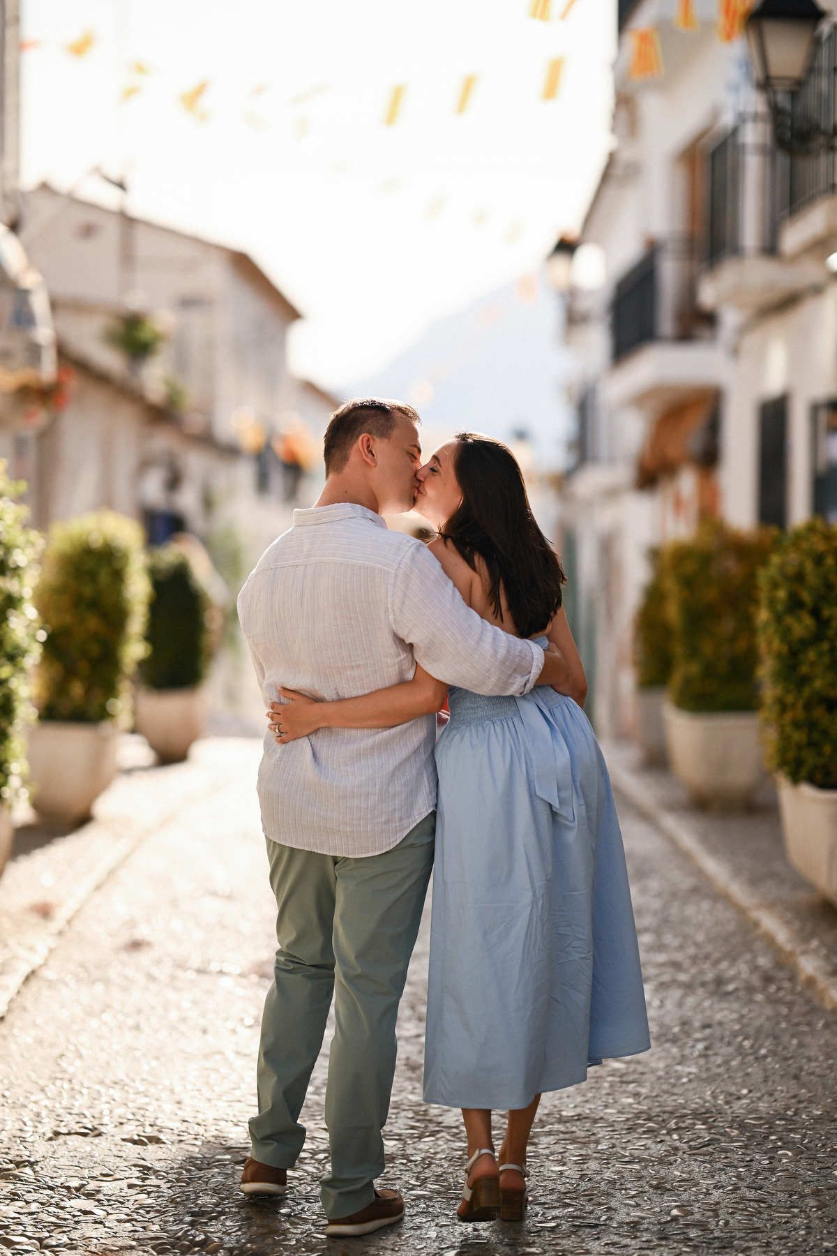 A couple kisses in a narrow whitewashed alley decorated with festive flags following their marriage proposal in Altea.