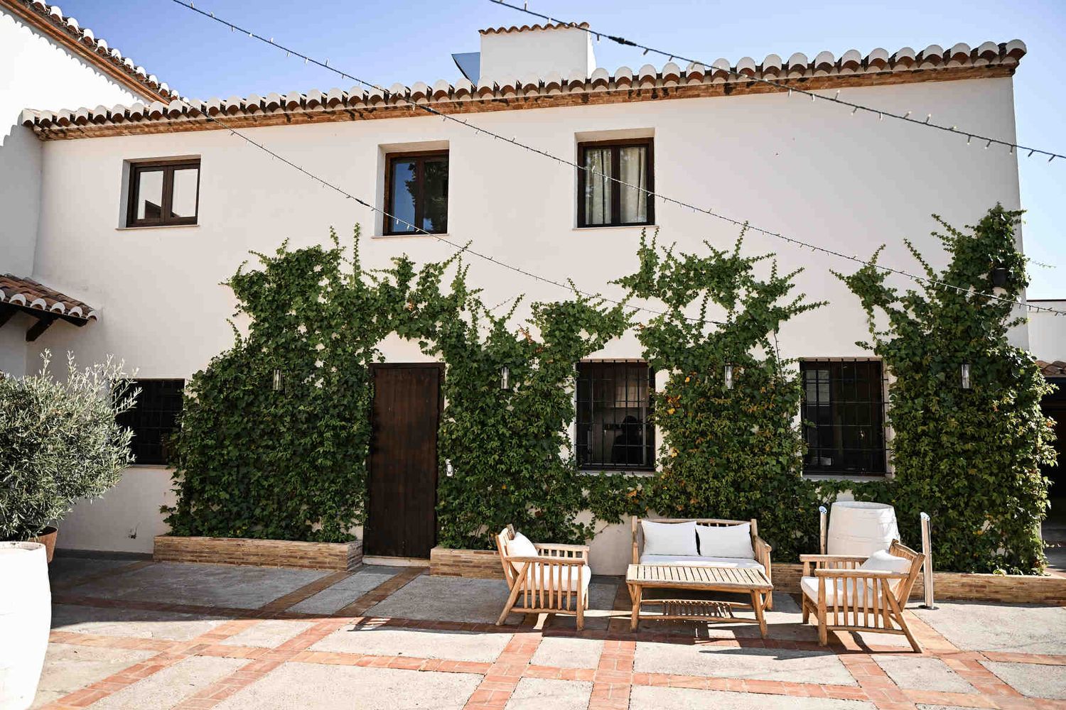 Patio de Arcos courtyard at Alquería Kukala with white-washed walls, climbing green ivy, and wooden lounge furniture.