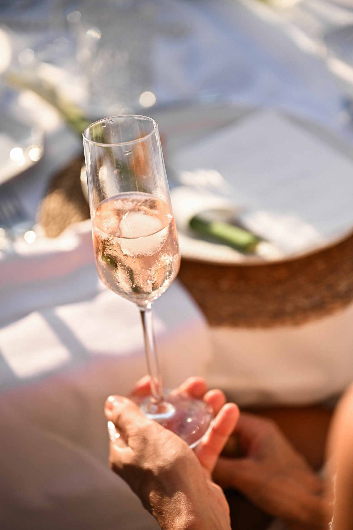 Close-up of a hand holding a glass of sparkling rose wine with ice at a wedding reception table.