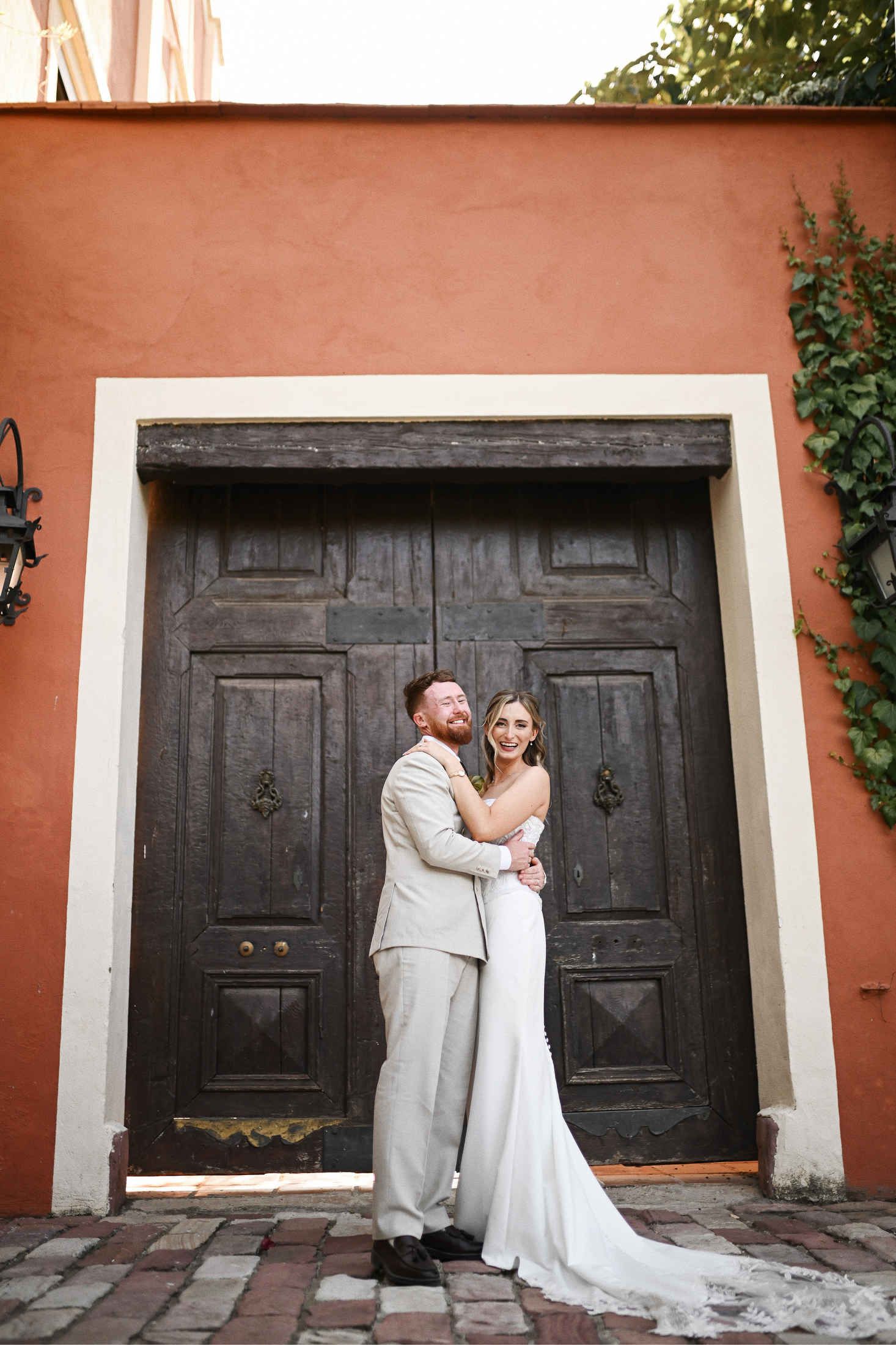 Bride and groom posing by the historic vintage wooden gates of Villa Dela wedding venue in Valencia, Spain.