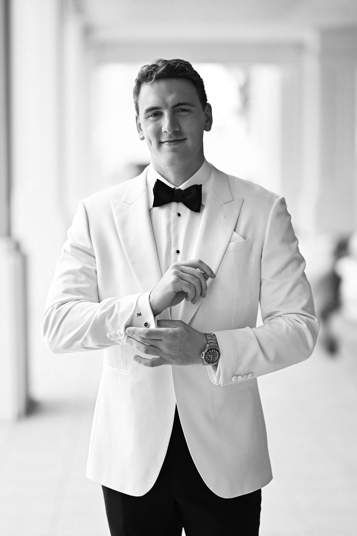 Black and white portrait of a groom in a white tuxedo adjusting his cufflinks at Hotel Las Arenas Valencia