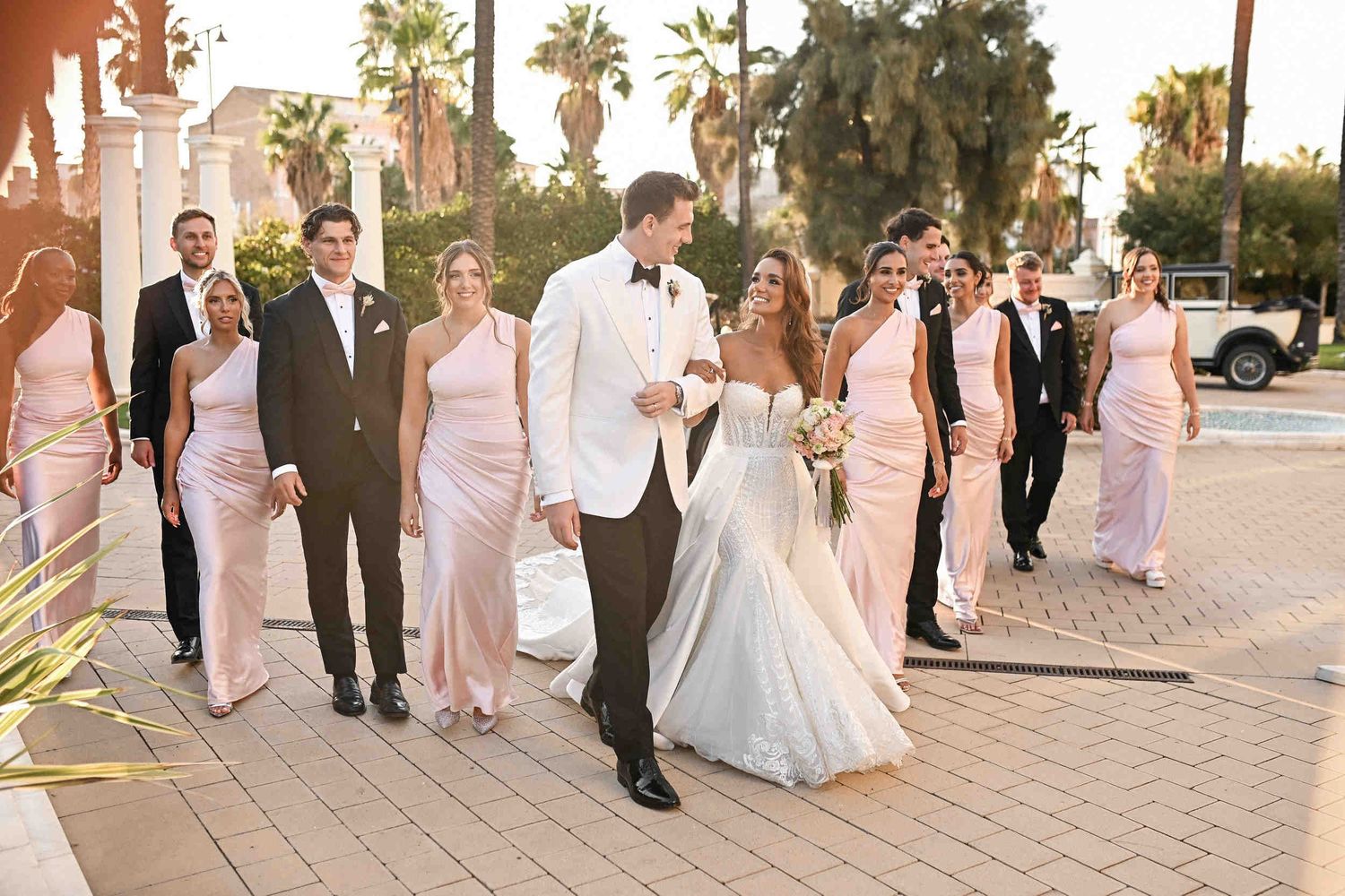 Bride and groom walking arm in arm with their wedding party through the sunny courtyard of Hotel Las Arenas Valencia