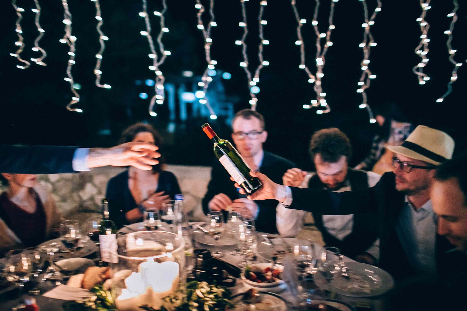 Candid documentary shot of guests sharing wine during a lively wedding dinner in Milos