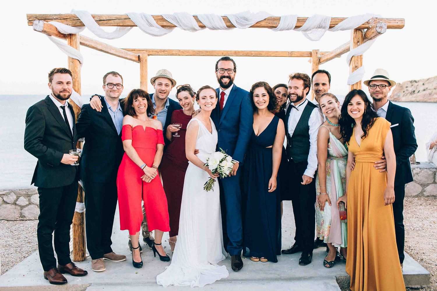 Joyful wedding guests gathering around the ceremony arch on the island of Milos.