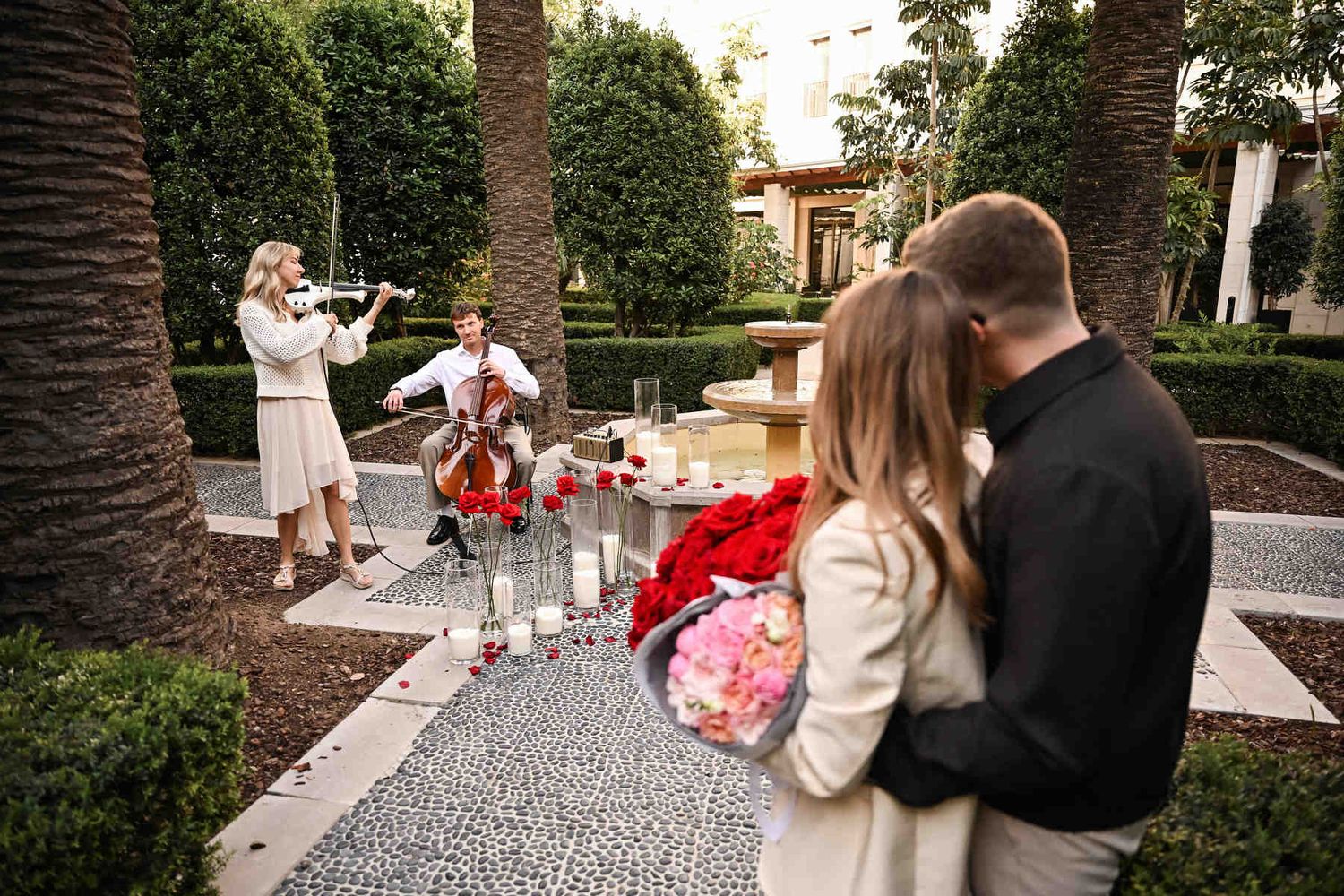 Engaged couple embracing and enjoying live cello and violin music in the garden after their surprise proposal in Valencia.