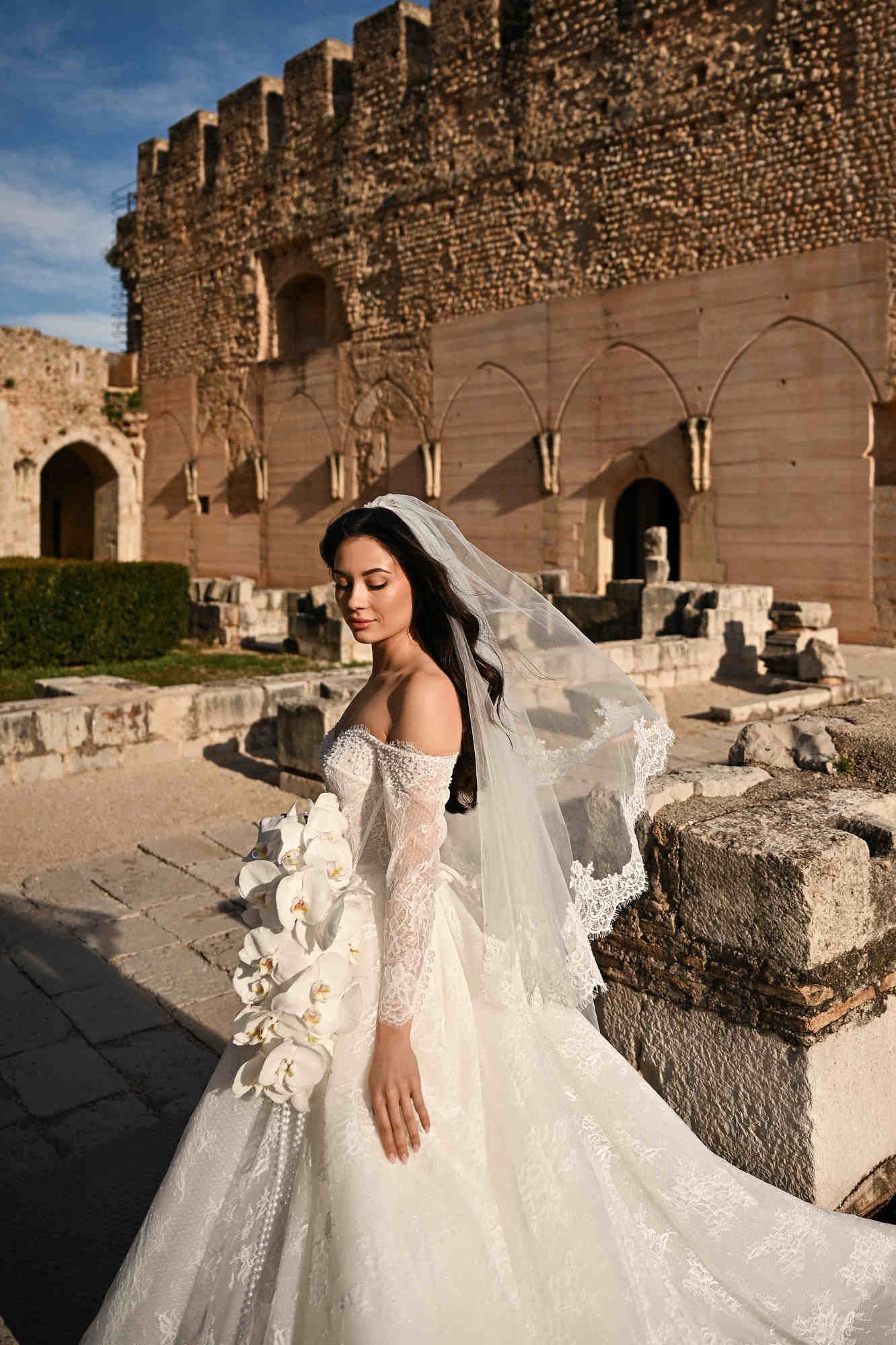 Close-up of a bride holding an orchid bouquet against the ancient stone walls of Monasterio de Santa María de la Valldigna in Valencia.