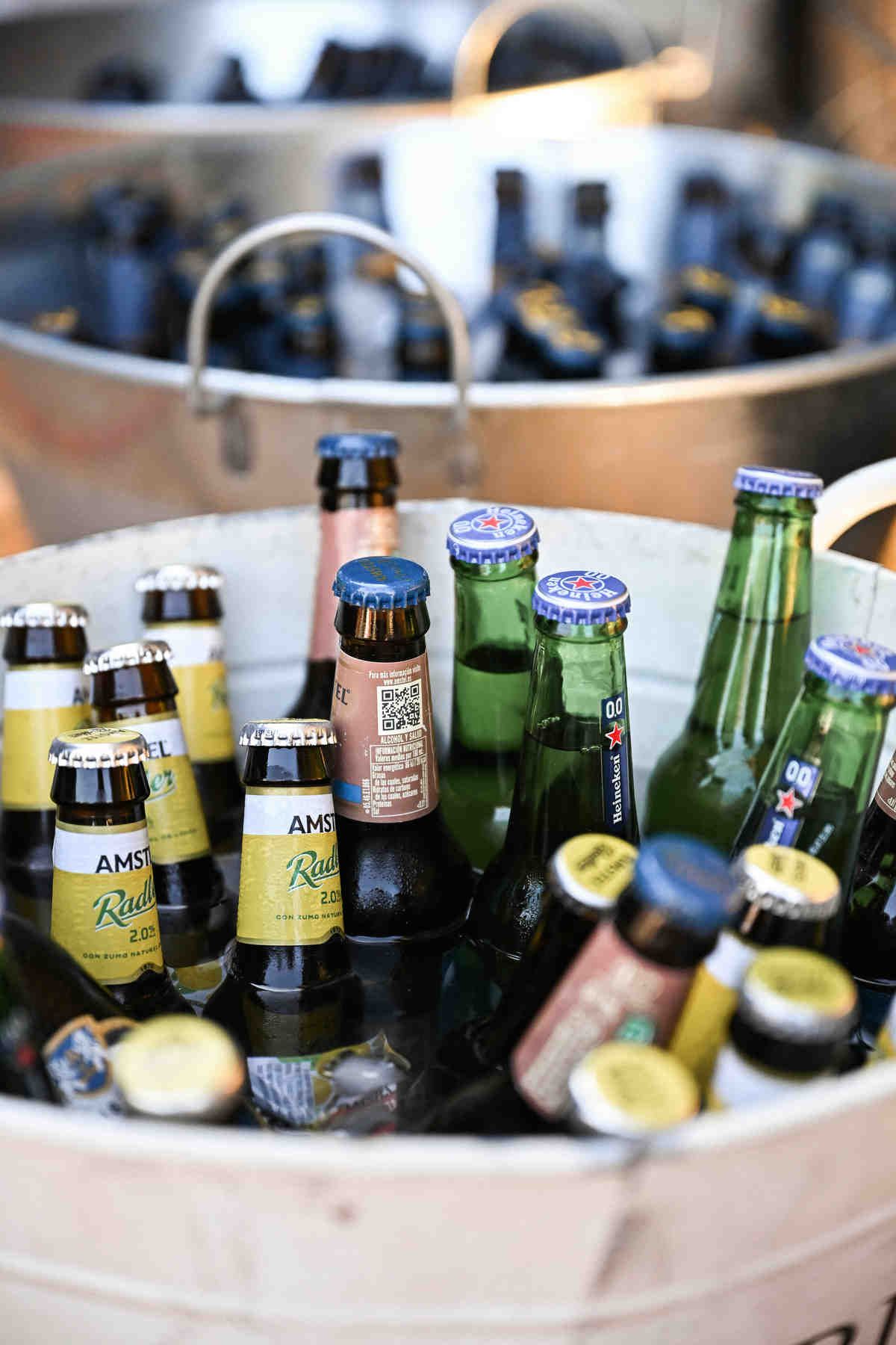 Chilled beer bottles in a metal ice bucket at an outdoor wedding cocktail reception in Spain.